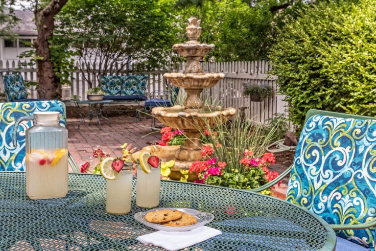 A pitcher of lemonade and two glasses sit on a table by a fountain in the outdoor courtyard of the Silver Heart Inn, the best Missouri Getaway for the summer,